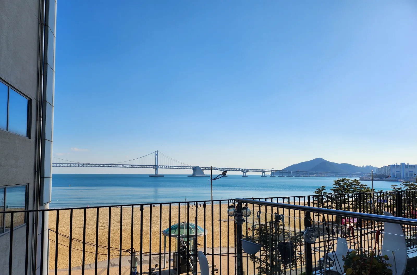 Gwangan Bridge across calm blue water, seen over a terrace railing above Gwangalli Beach on a clear January afternoon